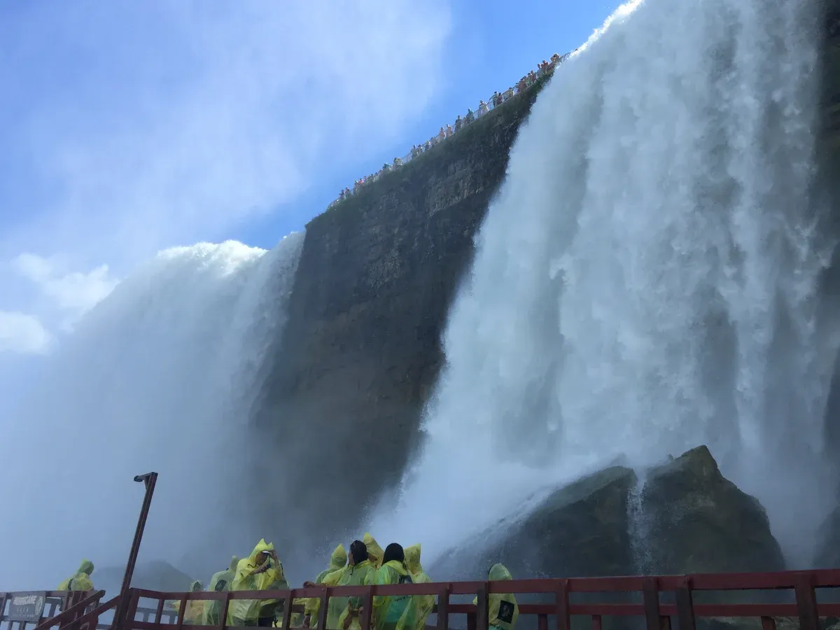 Visitors in yellow ponchos on the Hurricane Deck at the base of Bridal Veil Falls on a Niagara Falls tour from NYC, New York