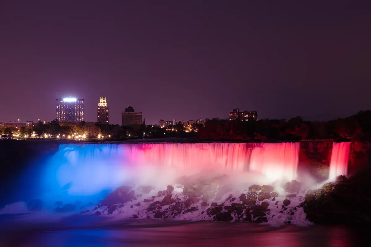 American Falls illuminated in colored lights at night on a Niagara Falls tour from NYC, New York
