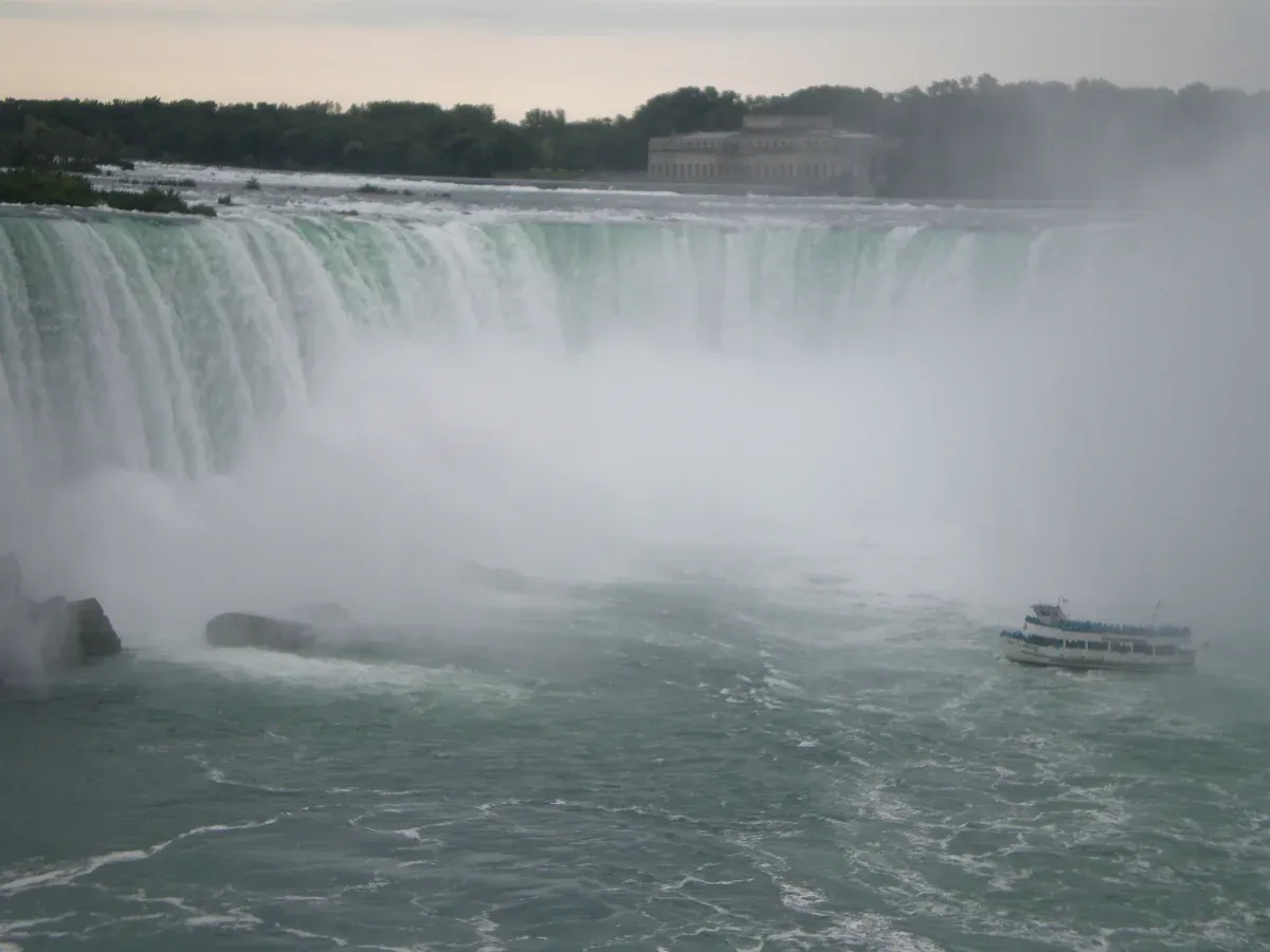 A Maid of the Mist boat with passengers in blue ponchos at the base of Horseshoe Falls on a Niagara Falls tour from NYC, New York